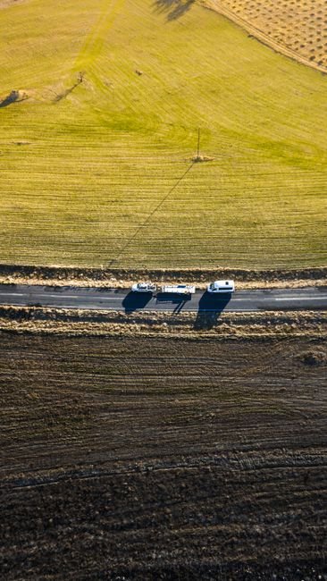 Camper trailer and tow vehicle on a flat rural highway through farm fields